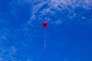 Un globo rojo con cinta blanca vuela en el cielo azul