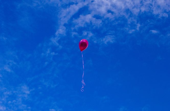 Un globo rojo con cinta blanca vuela en el cielo azul
